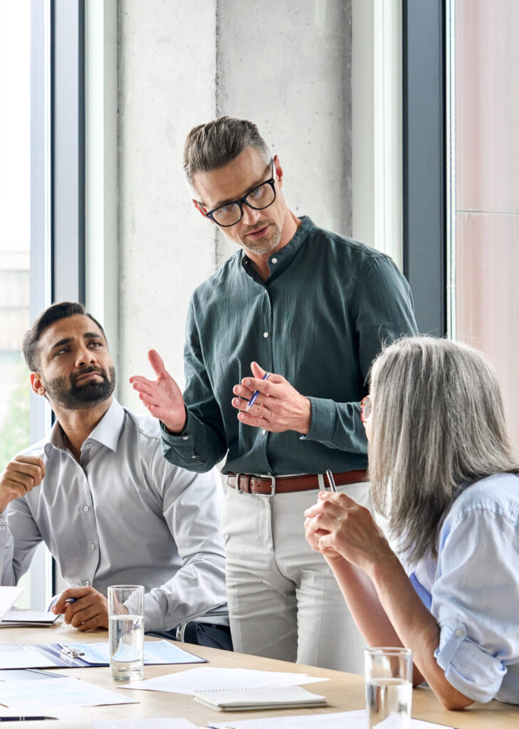 man standing beside two colleagues in front of desk at business meeting