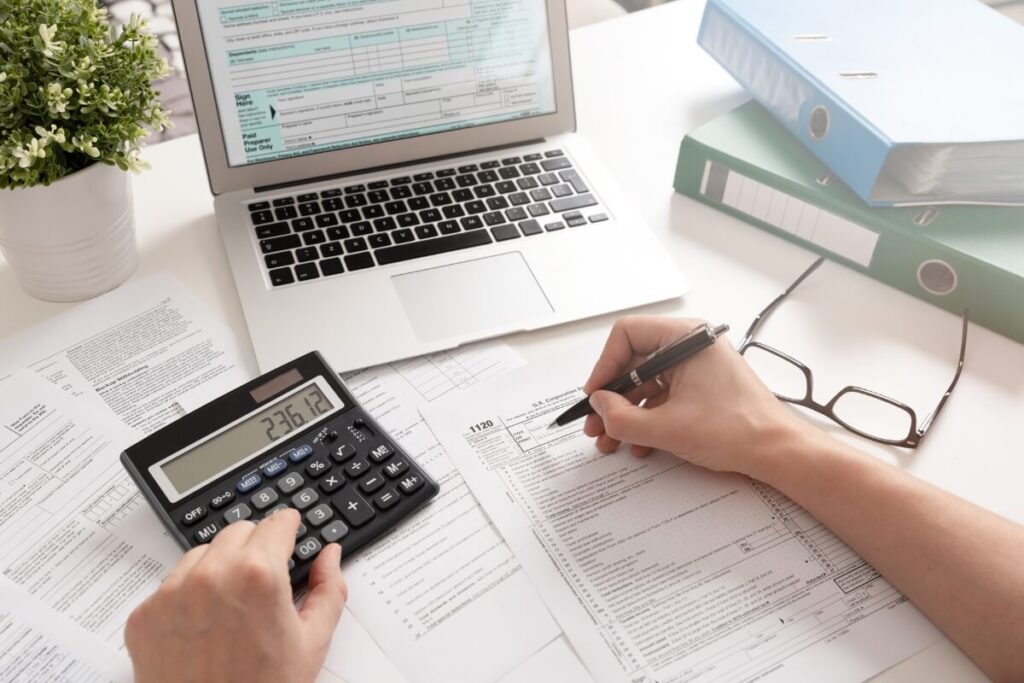 laptop and calculator on desk with person's hands doing ifrs accounting calculations