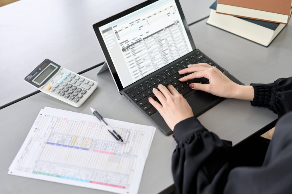 woman typing at laptop on gray desk with accounting spreadsheet open