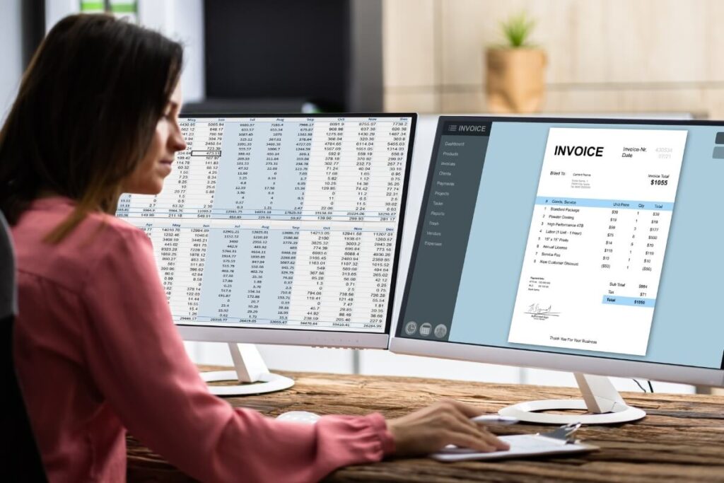 woman sitting at two computer monitors with accounting spreadsheet and invoice on screens